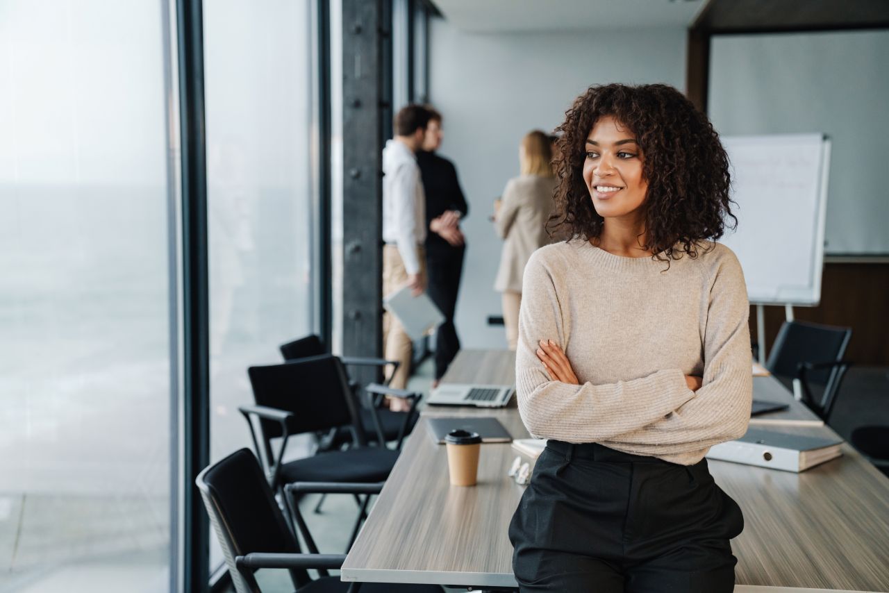 Woman employee with arms crossed leaning on desk