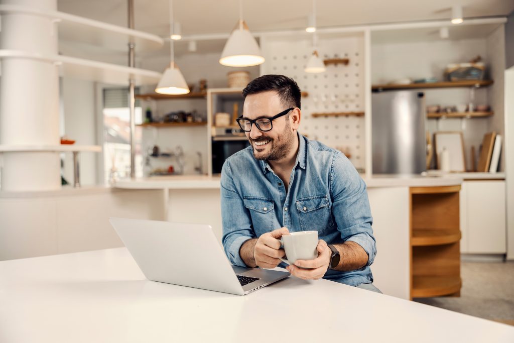 A happy man drinking coffee and looking at the laptop